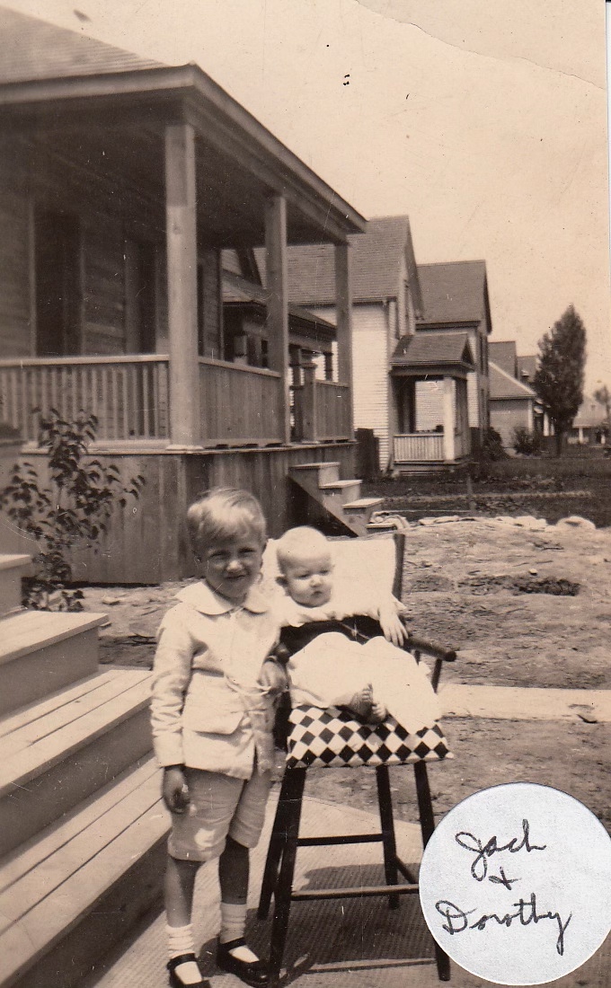 Baby in a wooden highchair, her older brother standing beside her